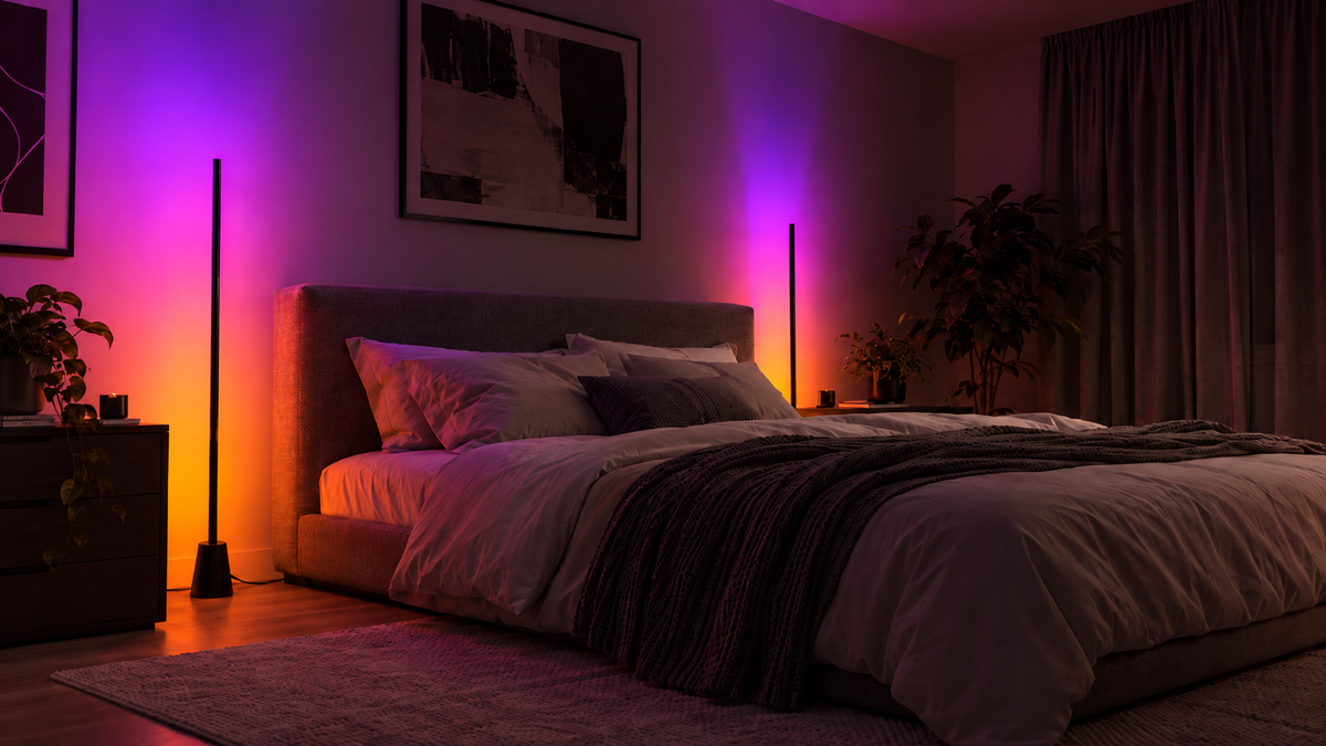 Modern bedroom with two slim black RGB floor lamps casting soft pink, purple and orange lighting around the bed.